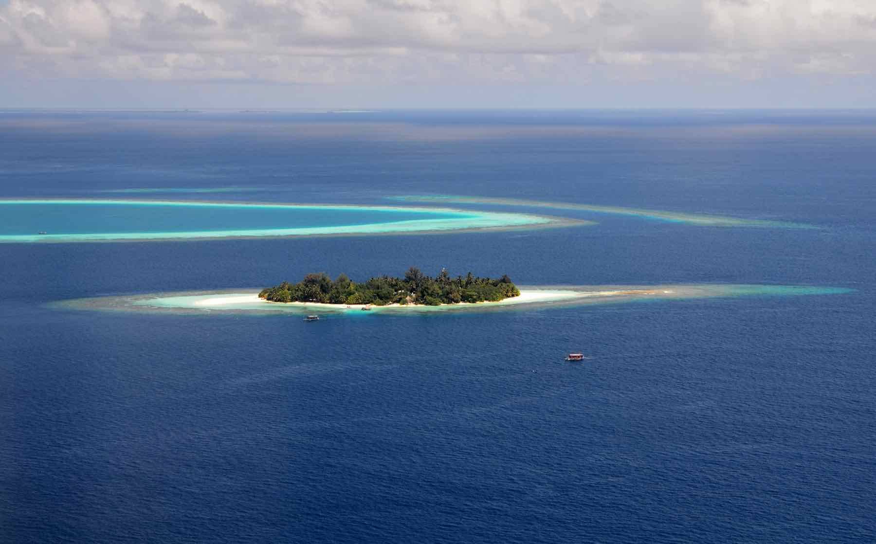 A Maldivian island ringed by a shallow lagoon, seen from the air